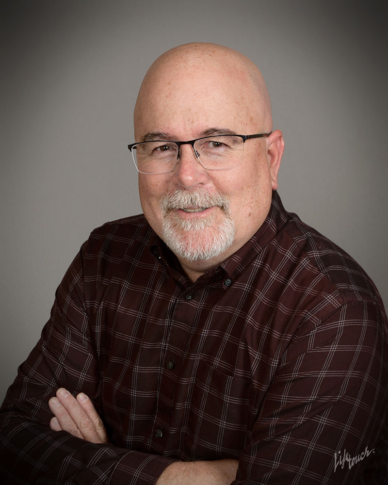 Rich Cook, CEO, Man in his 50's with a bald head and a gray goatee wearing a maroon plaid dress shirt